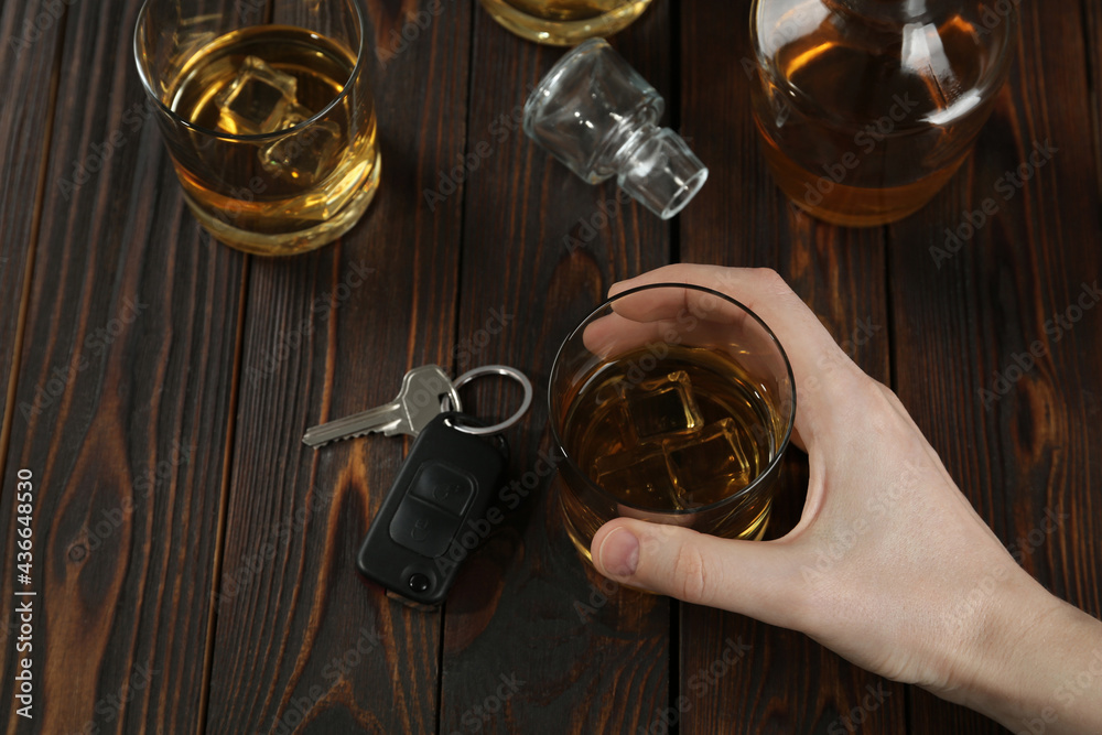 Man holding glass of alcohol near car key at wooden table, above view. Dangerous drinking and driving