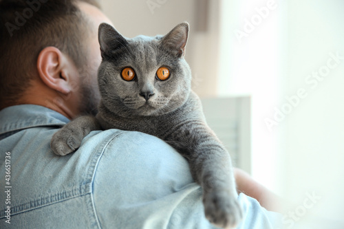 Man with cute cat on blurred background, closeup