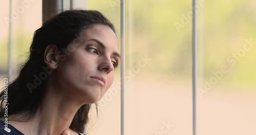 Close up head shot unhappy young hispanic latin caucasian woman looking out of window, feeling bored alone at home, suffering from solitude loneliness indoors, having psychological problems. photo