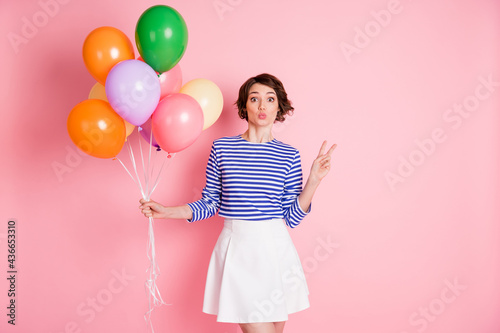 Photo of young beautiful attractive charming girl hold balloons pout lips showing v-sign isolated on pink color background © deagreez