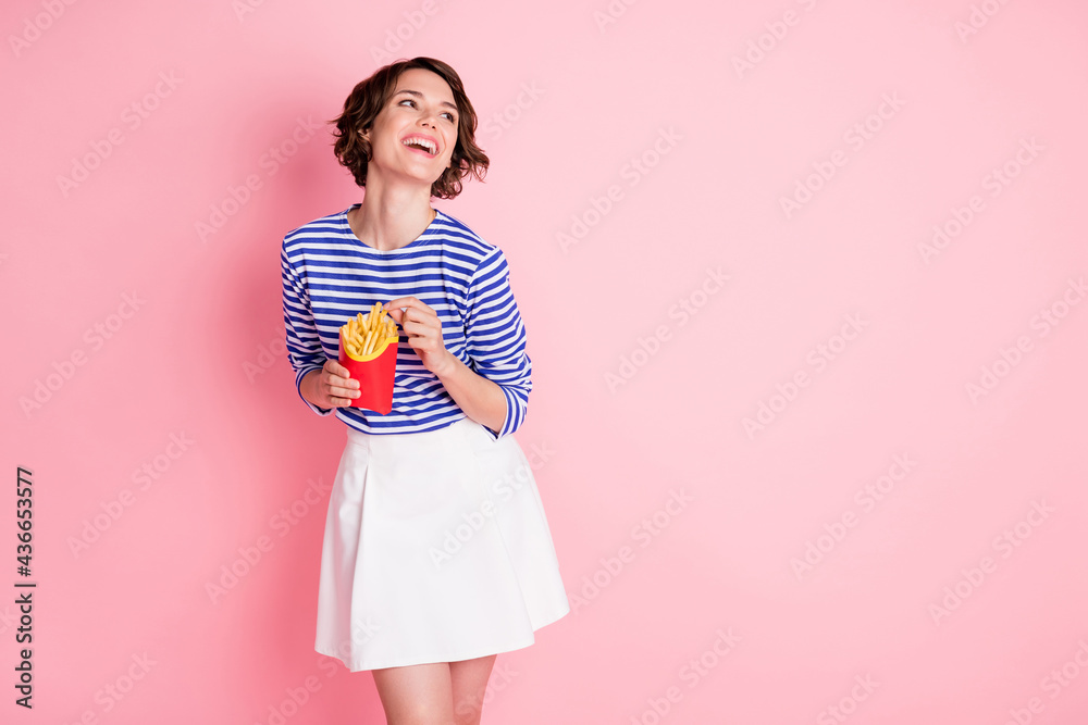 Photo of young attractive cheerful positive smiling girl look copyspace hold eat french fries isolated on pink color background Photo of young attractive cheerful positive smiling girl look copyspace hold eat french fries isolated on pink color background