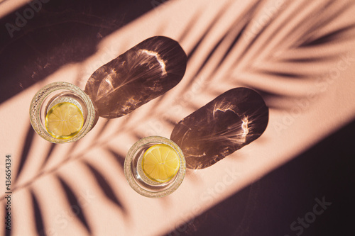 Two glasses of water with sliced lemon on sunlit background with shade. Summer refreshment concept. Minimal style.Top view. Flat lay