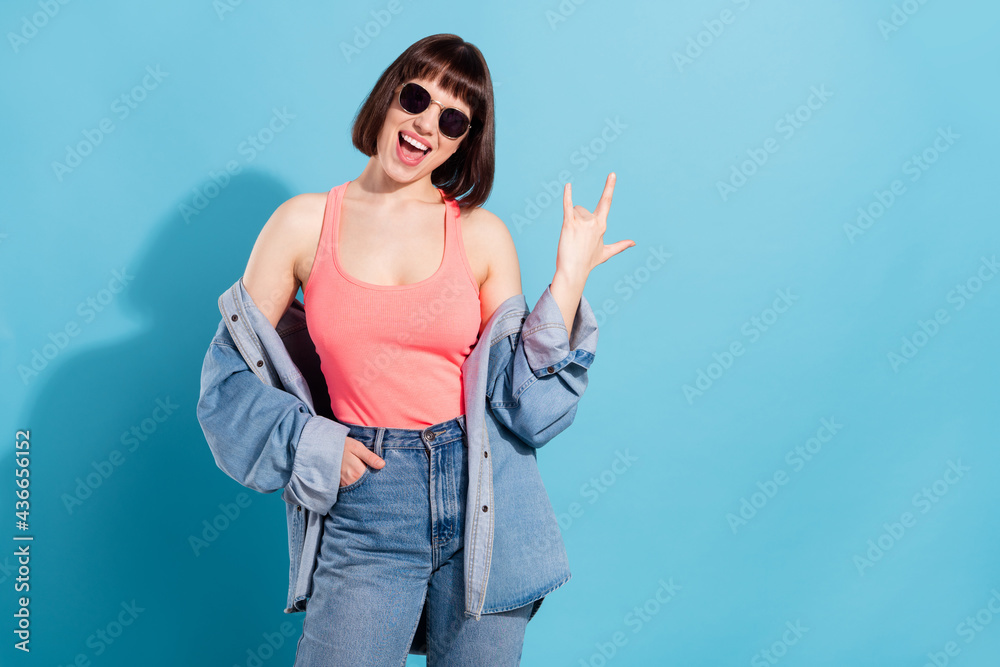 Photo of shiny horned lady dressed jeans shirt dark glasses showing fingers hard rock sign empty space isolated blue color background