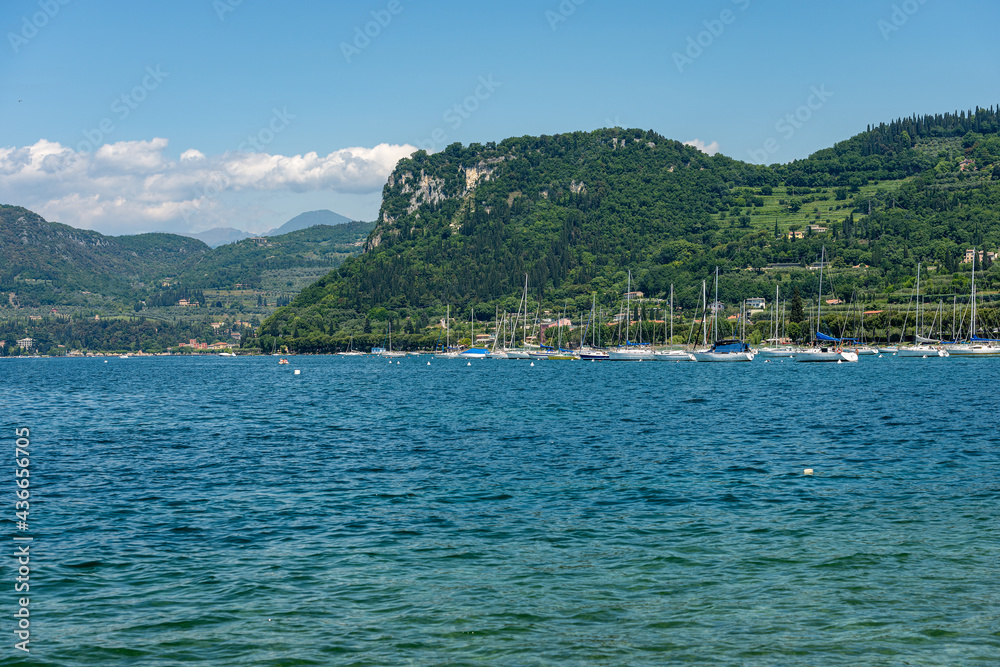 Large group of sailing boats moored in front of the small village of Bardolino, coast of Lake Garda (Lago di Garda) with the hill called Rocca di Garda. Verona province, Veneto, Italy, southern Europe