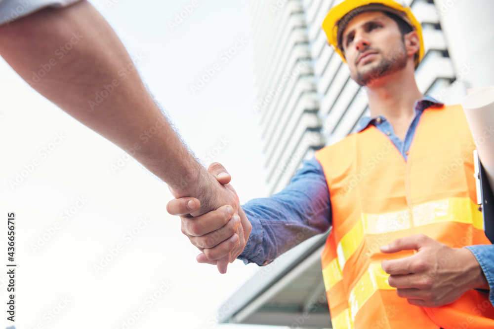 Portrait of engineer man giving an handshake in an industrial facility. Builder with blueprint shaking partner hand. architecture and home renovation concept Portrait of engineer man giving an handshake in an industrial facility. Builder with blueprint shaking partner hand. architecture and home renovation concept