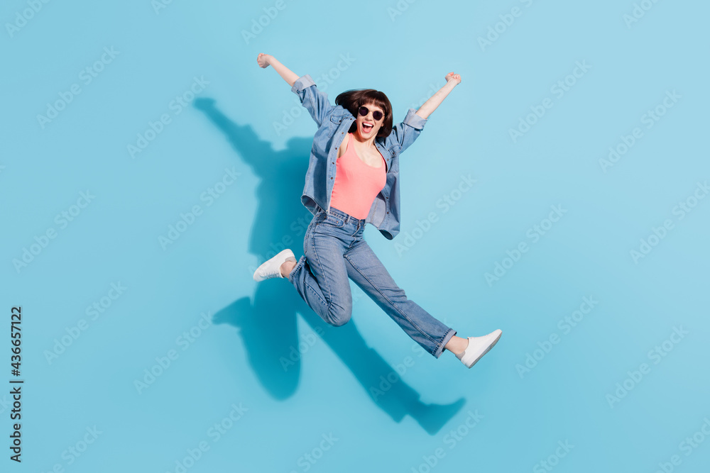 Full size photo of joyful young lady jump wear top jeans eyewear isolated on blue color background