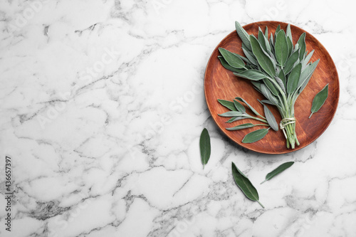 Wooden plate with fresh green sage on white marble  table, flat lay. Space for text photo