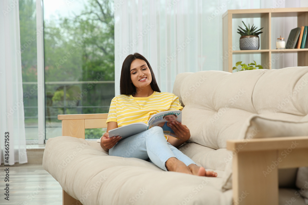 Young woman reading magazine on sofa at home Young woman reading magazine on sofa at home