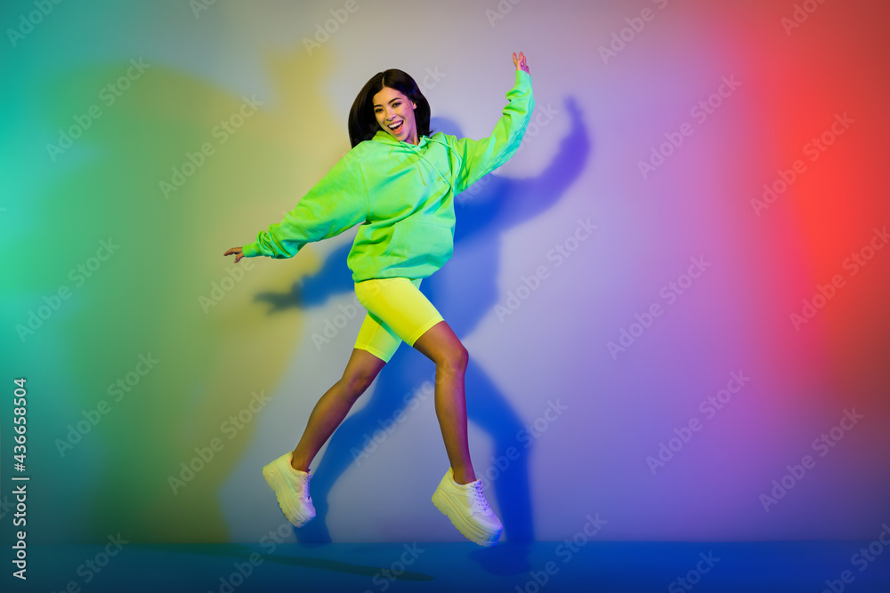 Full length body size view of pretty motivated cheerful girl jumping walking isolated over multicolor vivid neon light background Full length body size view of pretty motivated cheerful girl jumping walking isolated over multicolor vivid neon light background