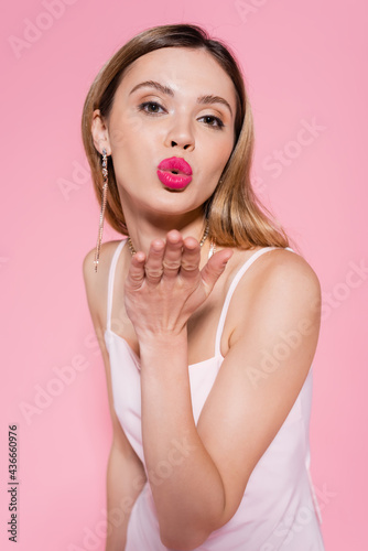 Pretty woman blowing air kiss at camera isolated on pink.