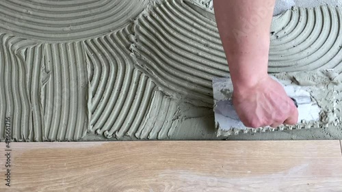 A tiler applies adhesive to the floor to install ceramic tiles. Laying tiles at a construction site. Selective focus, plenty of copy space 