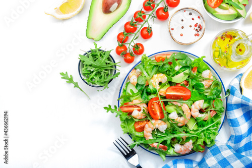 Summer shrimp salad with tomatoes, lettuce, arugula, avocado, cucumber and lemon dressing on white background. Healthy eating, clean food