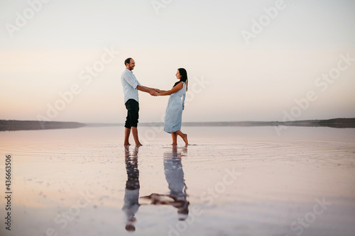 Side view of attractive young couple holding on their hands and standing on the beach. Concept of harmony relationships.