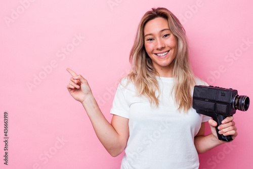 Young australian woman filming with a vintage video camera isolated smiling and pointing aside, showing something at blank space.