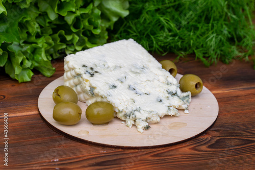 Piece of French Roquefort cheese with olives and fresh herbs