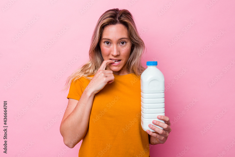 Young australian woman holding a bottle of milk isolated on pink background biting fingernails, nervous and very anxious. Young australian woman holding a bottle of milk isolated on pink background biting fingernails, nervous and very anxious.