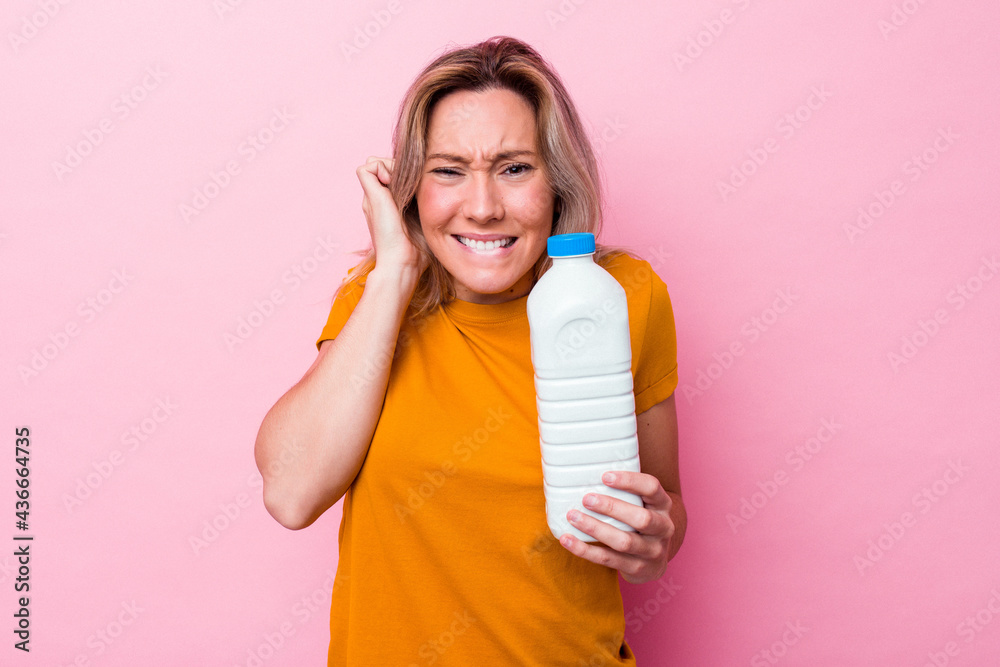 Young australian woman holding a bottle of milk isolated on pink background covering ears with hands. Young australian woman holding a bottle of milk isolated on pink background covering ears with hands.