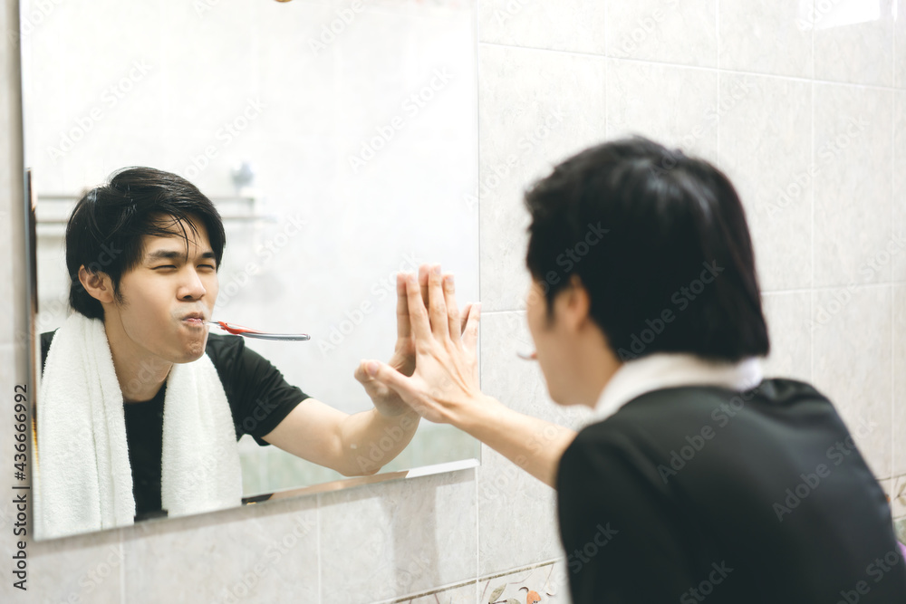 Young adult asian man brushing teeth in font of bathroom mirror and self awareness practice. Young adult asian man brushing teeth in font of bathroom mirror and self awareness practice.