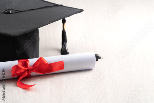 Graduation academic cap with diploma on wooden table background.