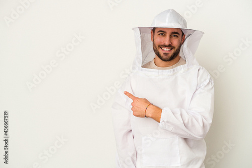 фотографія Young apiculture caucasian man isolated on white background smiling and pointing aside, showing something at blank space