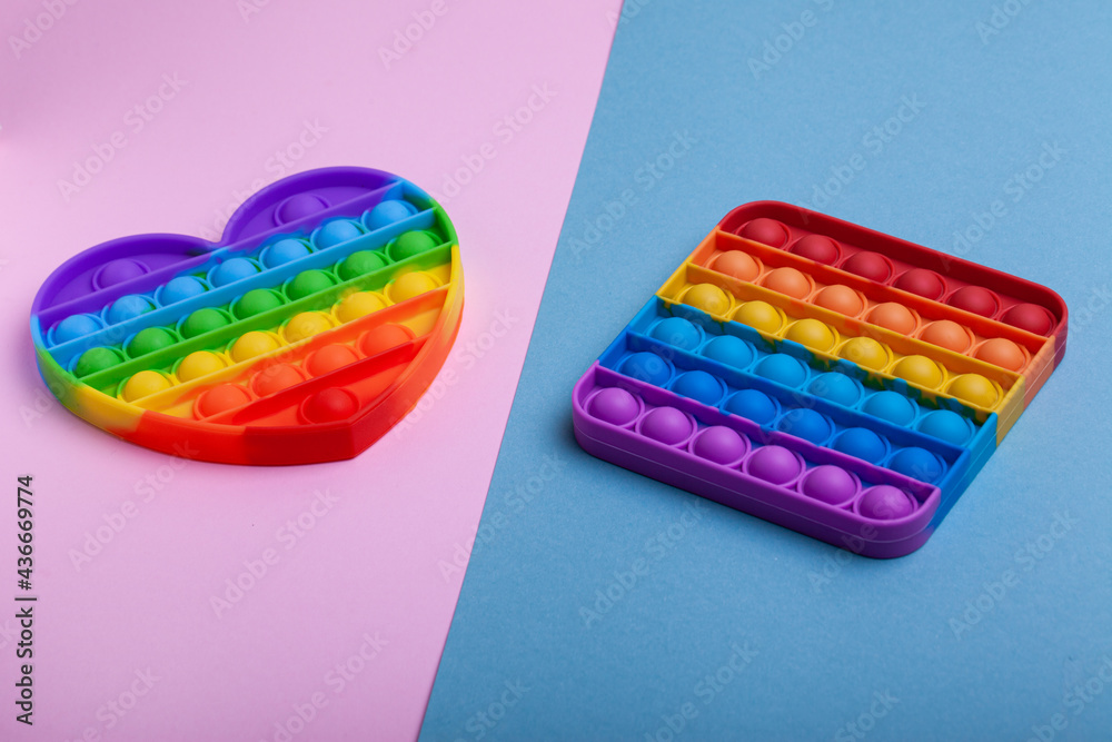 Rainbow heart and square shape Pop it fidget toy om pastel background. Simple dimple toy on pink and blue pastel background. Rainbow heart and square shape Pop it fidget toy om pastel background. Simple dimple toy on pink and blue pastel background.