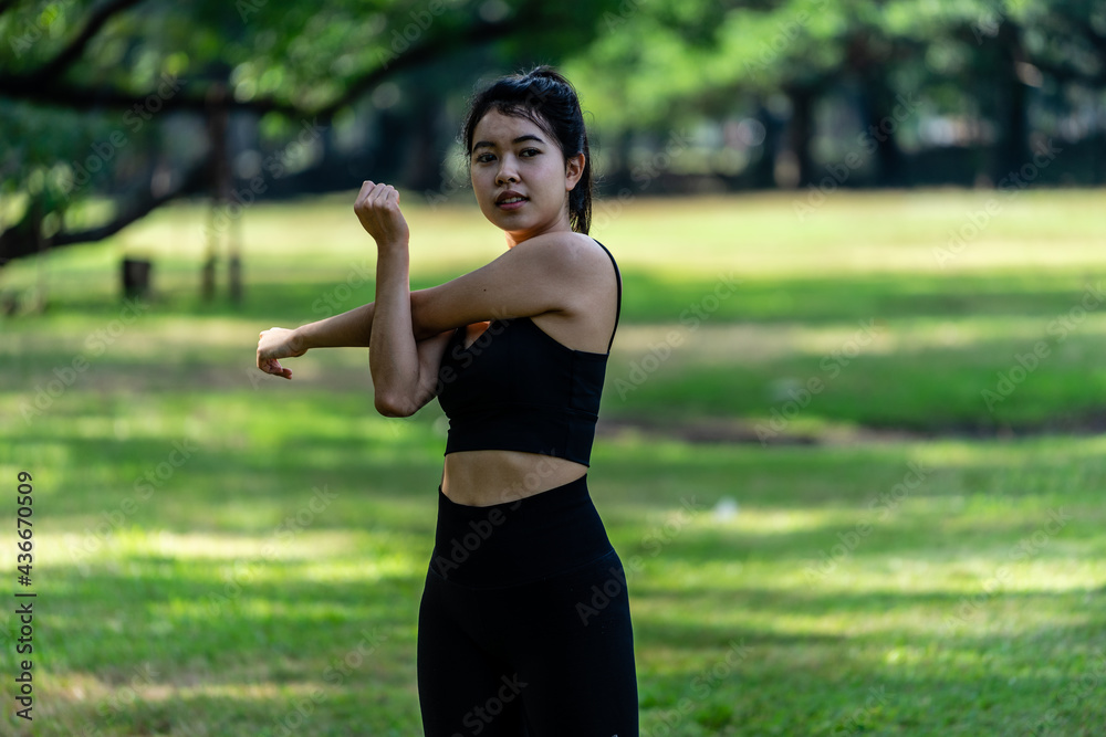 Asian woman wearing tight exercise clothes are doing exercises by twist her body with arms in public park Asian woman wearing tight exercise clothes are doing exercises by twist her body with arms in public park