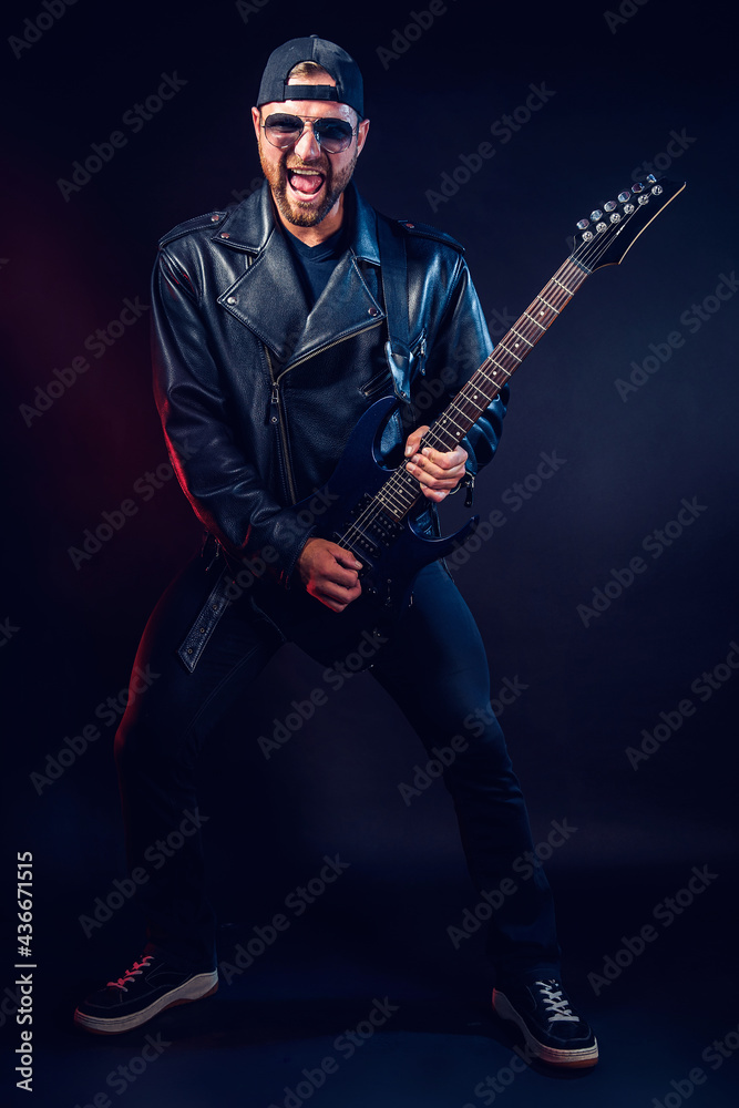 Full size photo of brutal bearded Heavy metal musician in leather jacket and sunglasses is playing electrical guitar very emotionally. Shot in a studio on dark background Full size photo of brutal bearded Heavy metal musician in leather jacket and sunglasses is playing electrical guitar very emotionally. Shot in a studio on dark background
