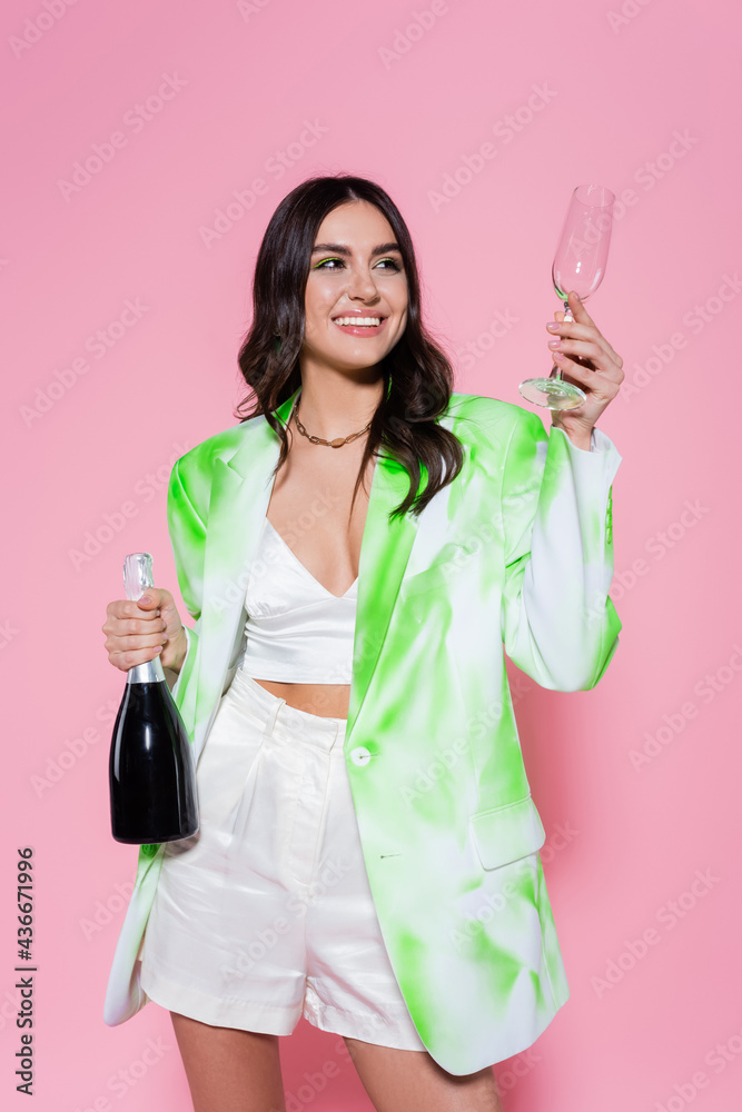 Smiling woman holding glass and bottle of champagne on pink background. Smiling woman holding glass and bottle of champagne on pink background.
