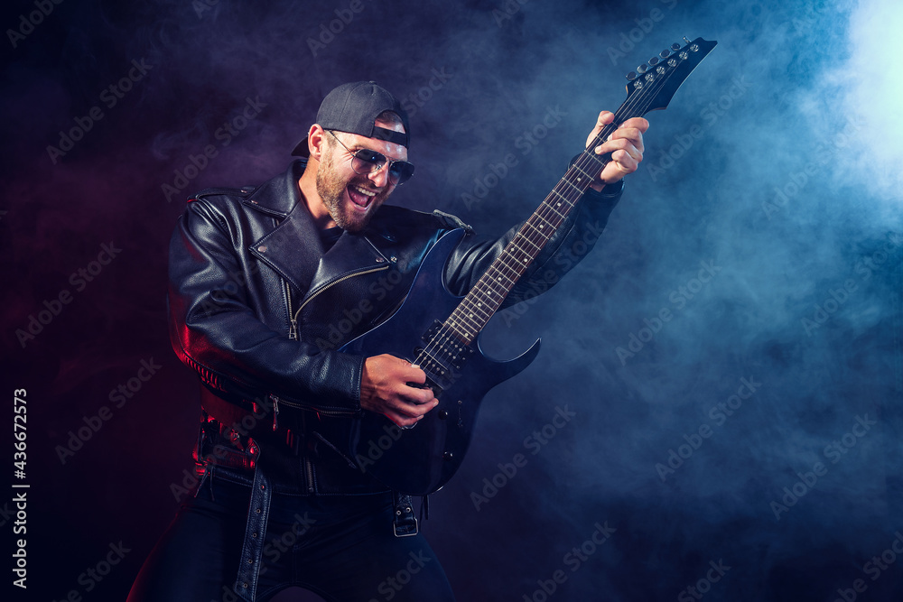 Brutal bearded Heavy metal musician in leather jacket and sunglasses is playing electrical guitar. Shot in a studio on dark background with smoke Brutal bearded Heavy metal musician in leather jacket and sunglasses is playing electrical guitar. Shot in a studio on dark background with smoke