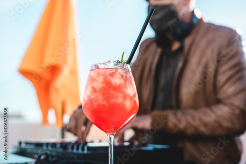 Close up of a special cocktail at beach party - Dj playing music at cocktail bar outdoor wearing safety face mask for coronavirus outbreak - Entertainment and party concept - Focus on cocktail