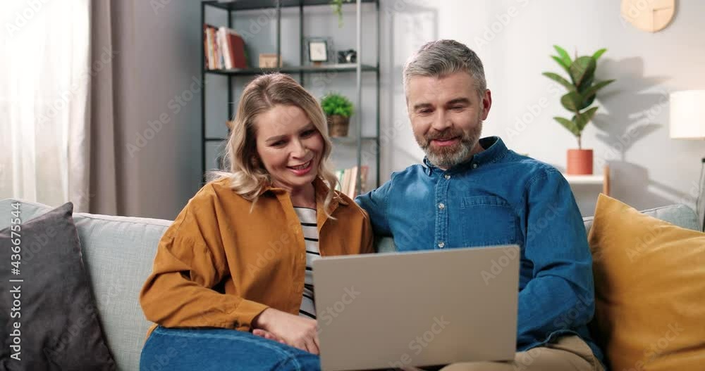 Portrait of joyful happy Caucasian middle-aged adult family couple wife and husband speaking on video call online on laptop computer in positive mood resting on sofa in cozy room at home, video chat Portrait of joyful happy Caucasian middle-aged adult family couple wife and husband speaking on video call online on laptop computer in positive mood resting on sofa in cozy room at home, video chat