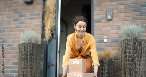 Young woman happy to receive parcels which were left by the courier contactless on the porch in front of the house. Concept of home delivery during a pandemic