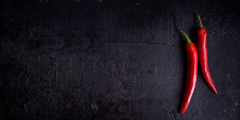 Red hot chili peppers on black rustic textured slate from above. Food background with spicy chilli paprika.