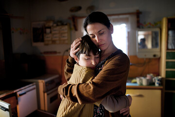 Portrait of sad poor mature mother hugging small daughter indoors at home, poverty concept.