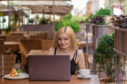 young blonde woman sitting with a laptop on summer terrace. front view