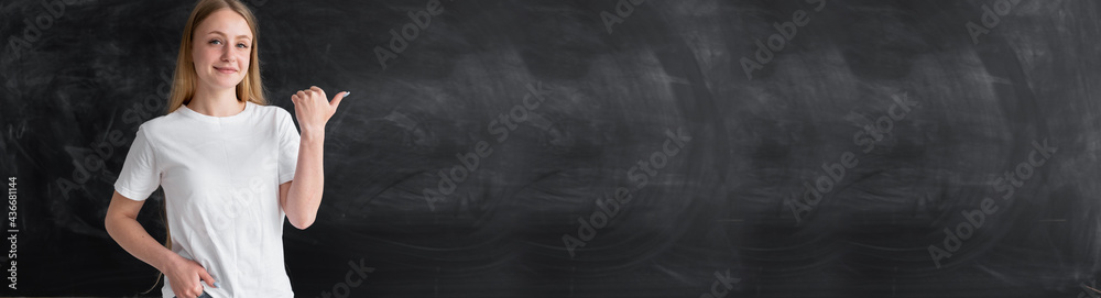 Caucasian woman teacher or student standing in front of the blackboard shows the place for the text. Banner. Clean chalk board. School and subjects concept. Caucasian woman teacher or student standing in front of the blackboard shows the place for the text. Banner. Clean chalk board. School and subjects concept.