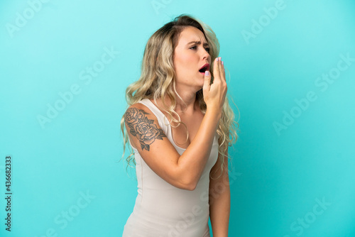 Young Brazilian woman isolated on blue background yawning and covering wide open mouth with hand