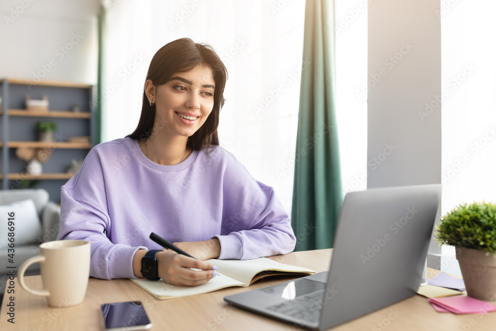 Woman sitting at desk, using computer writing in notebook Woman sitting at desk, using computer writing in notebook