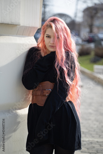 a girl with long pink hair stands up and looks into the lens, she is wearing a Basco belt