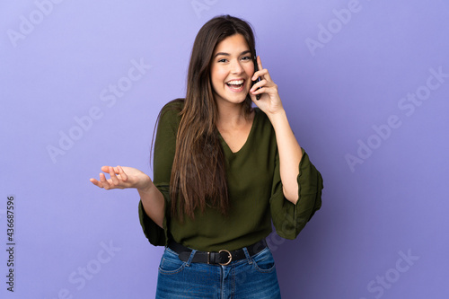 Teenager Brazilian girl over isolated purple background keeping a conversation with the mobile phone with someone