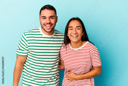 Young mixed race couple isolated on blue background laughing and having fun.