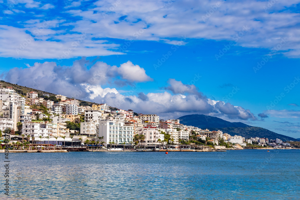 Panoramic view of Saranda bay and town and hotels along the coast, Albania. Sunny summer day. Beautiful clouds in the sky. Albanian mountains visible on the horizon. Calm blue sea.