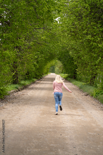The girl blonde on the road runs in a tree arch
