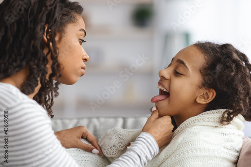 Little girl suffering from tonsillitis, mother checking her throat