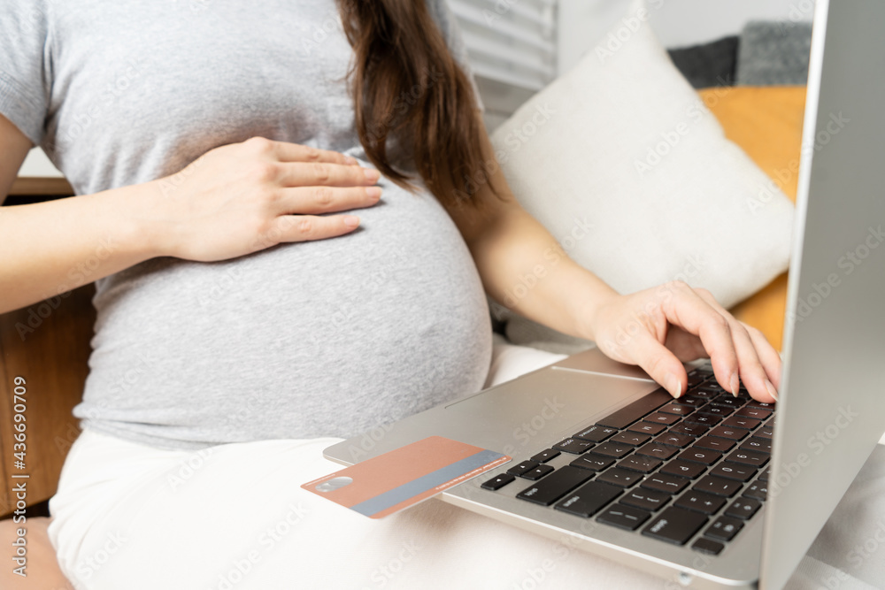 Fototapeta premium Online shopping on the Internet. Pregnant girl at the computer, pays for children's shopping with a card