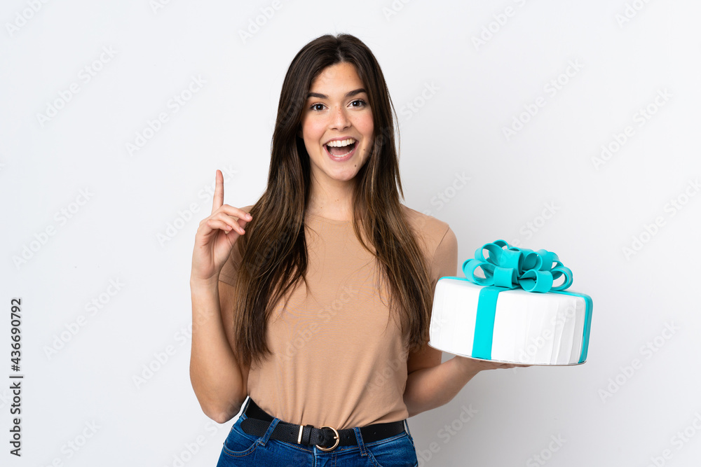Teenager pastry chef holding a big cake over isolated white background pointing up a great idea Teenager pastry chef holding a big cake over isolated white background pointing up a great idea