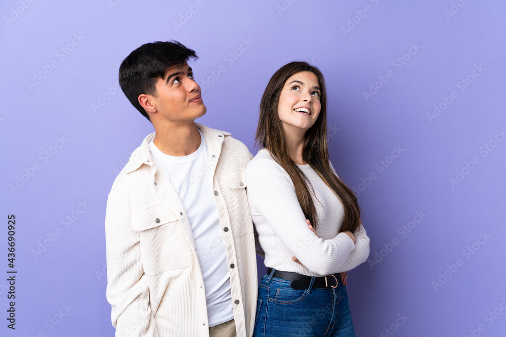 Young couple over isolated purple background looking up while smiling Young couple over isolated purple background looking up while smiling