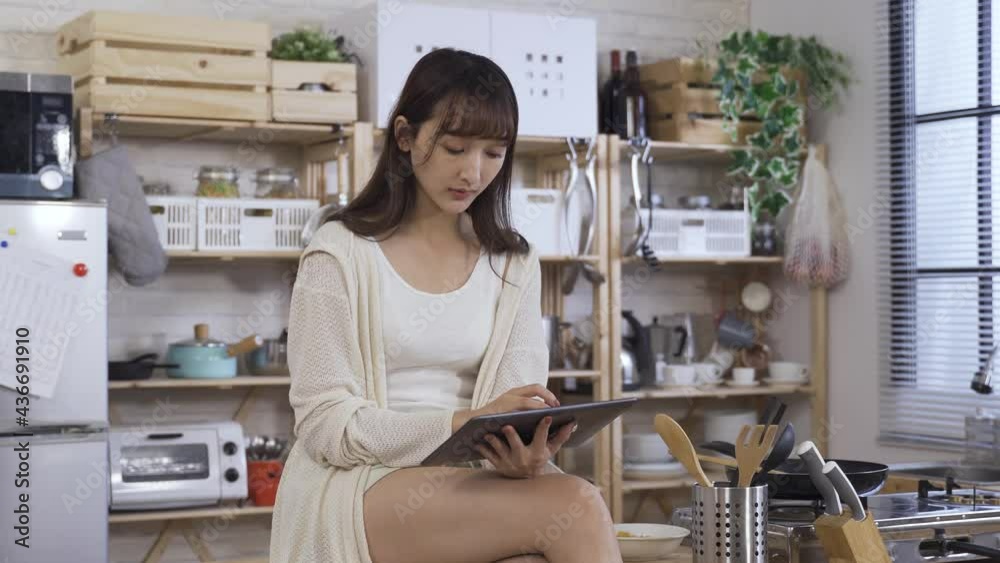 concentrated girl siting on the kitchen table is tapping and sliding on the screen while studying something with a touchpad in hands at home. concentrated girl siting on the kitchen table is tapping and sliding on the screen while studying something with a touchpad in hands at home.