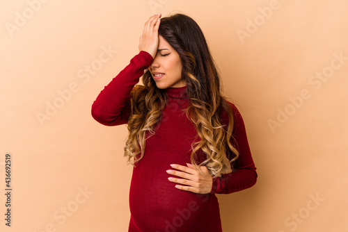 Young mexican pregnant woman isolated on beige background forgetting something, slapping forehead with palm and closing eyes. © Asier