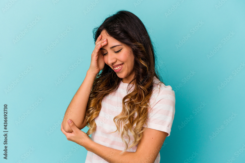 Young mexican woman isolated on blue background blink at the camera through fingers, embarrassed covering face.